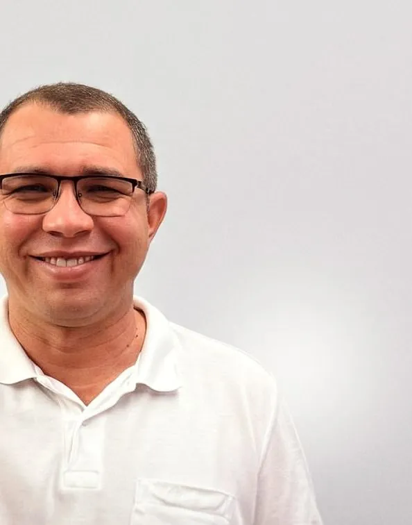 Retrato de Etniel Anchieta de camisa polo branca, sorrindo e apontando para a câmera.